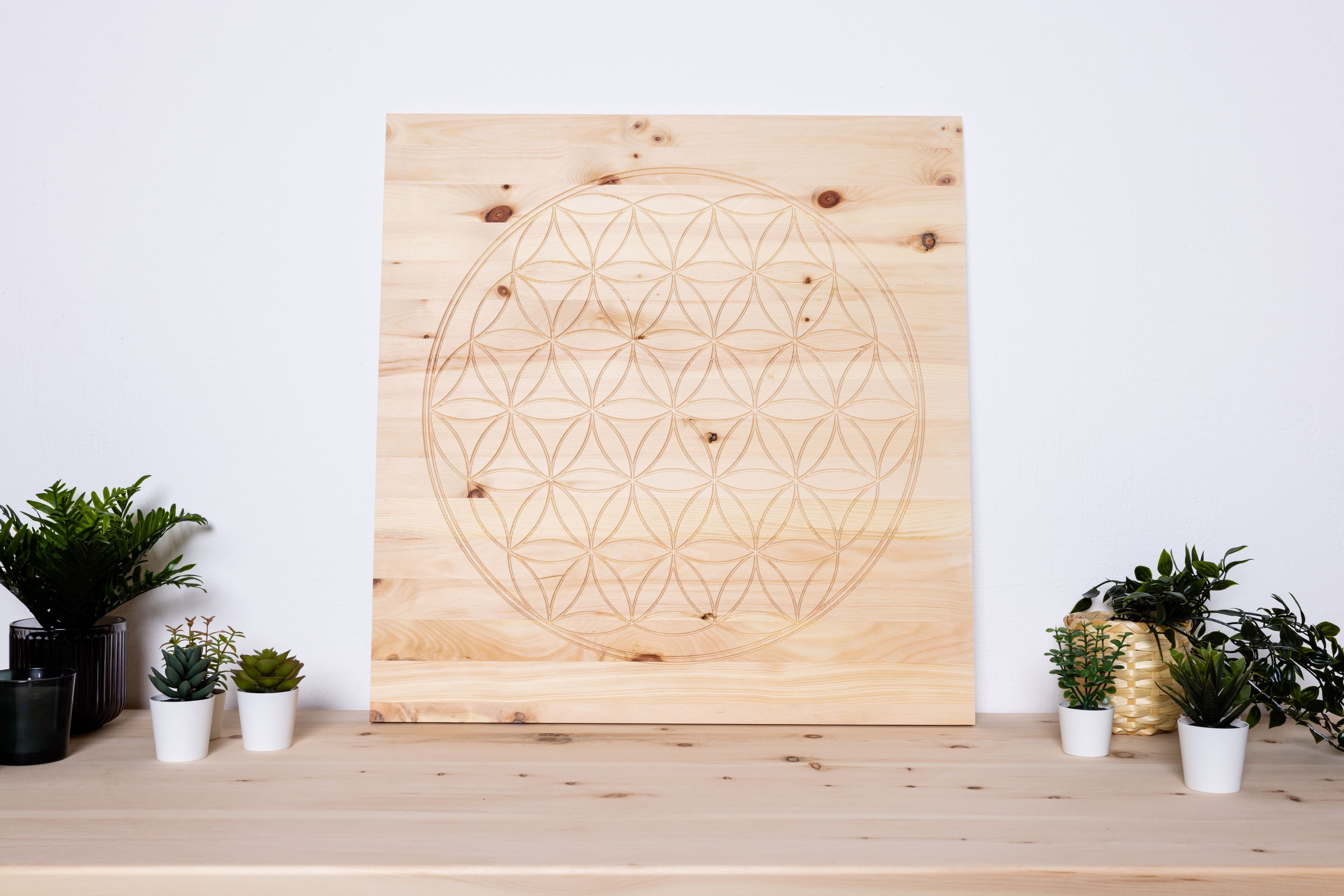 Wandbild aus Zirbenholz mit geometrischem Muster auf einem Tisch mit Pflanzen.