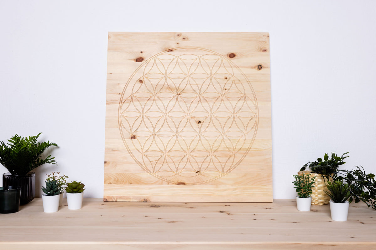 Wandbild aus Zirbenholz mit geometrischem Muster auf einem Tisch mit Pflanzen.